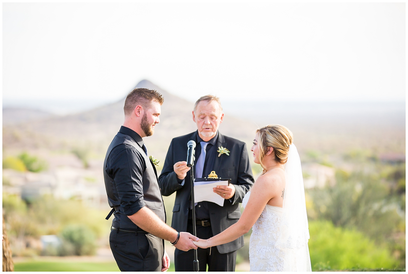 bride with fishtail braid and strapless dress with white rose and greenery bouquet with groom in black pants and vest and tie with rolled up shirt sleeves with succulent boutonniere during outdoor wedding ceremony