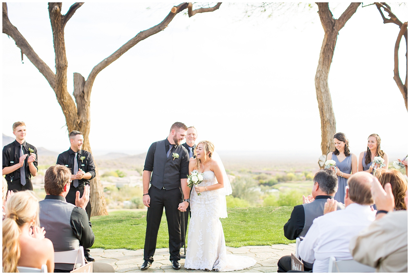 bride with fishtail braid and strapless dress with white rose and greenery bouquet with groom in black pants and vest and tie with rolled up shirt sleeves with succulent boutonniere during outdoor wedding ceremony