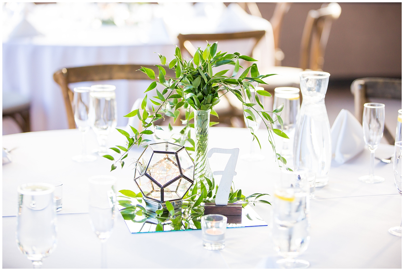 geometric terranium on mirror with glass vase with greenery and succulents with white table number and wood chairs in ballroom wedding reception details