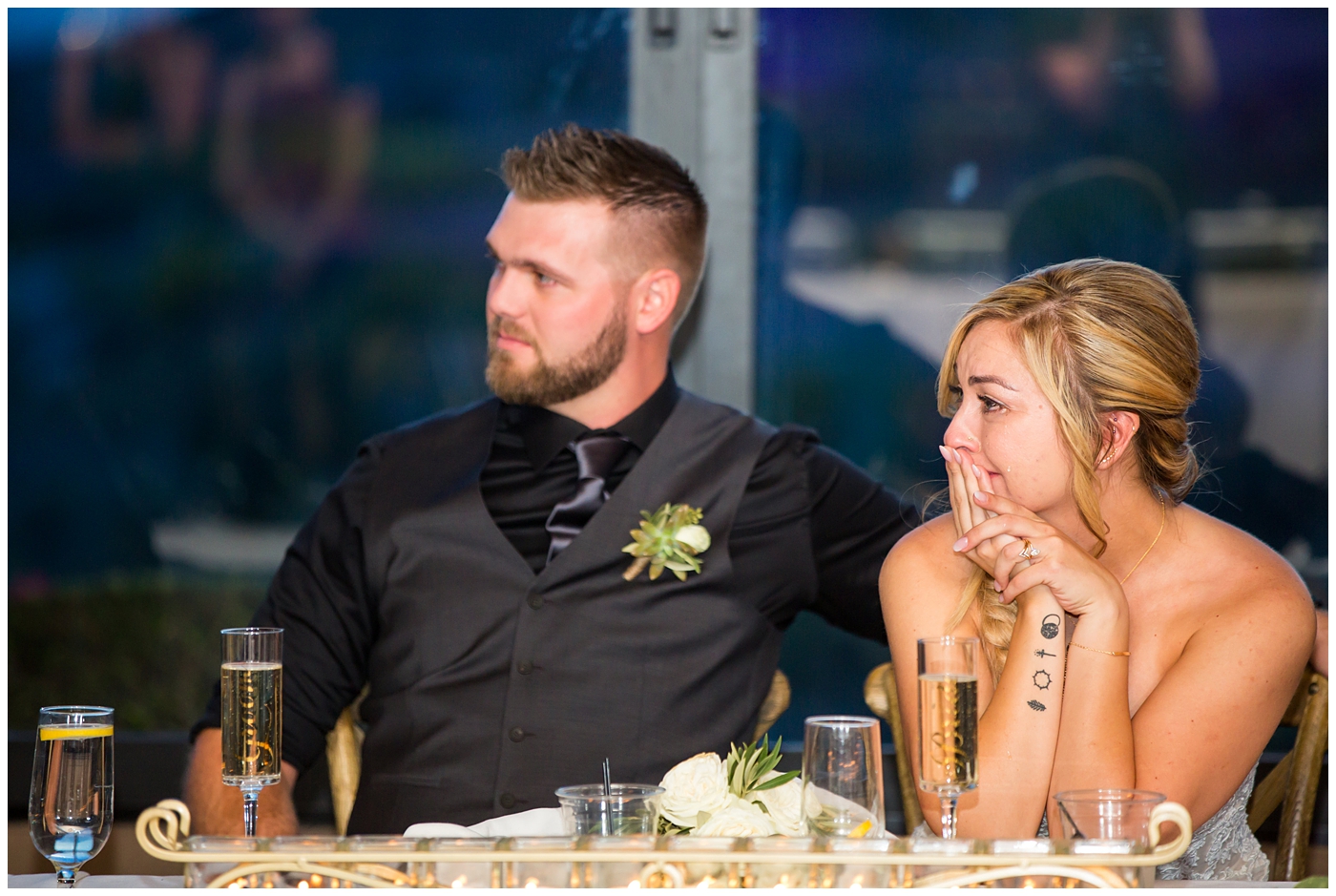 bride with fishtail braid and strapless dress with white rose and greenery bouquet with groom in black pants and vest and tie with rolled up shirt sleeves with succulent boutonniere wedding day portrait at reception during toasts
