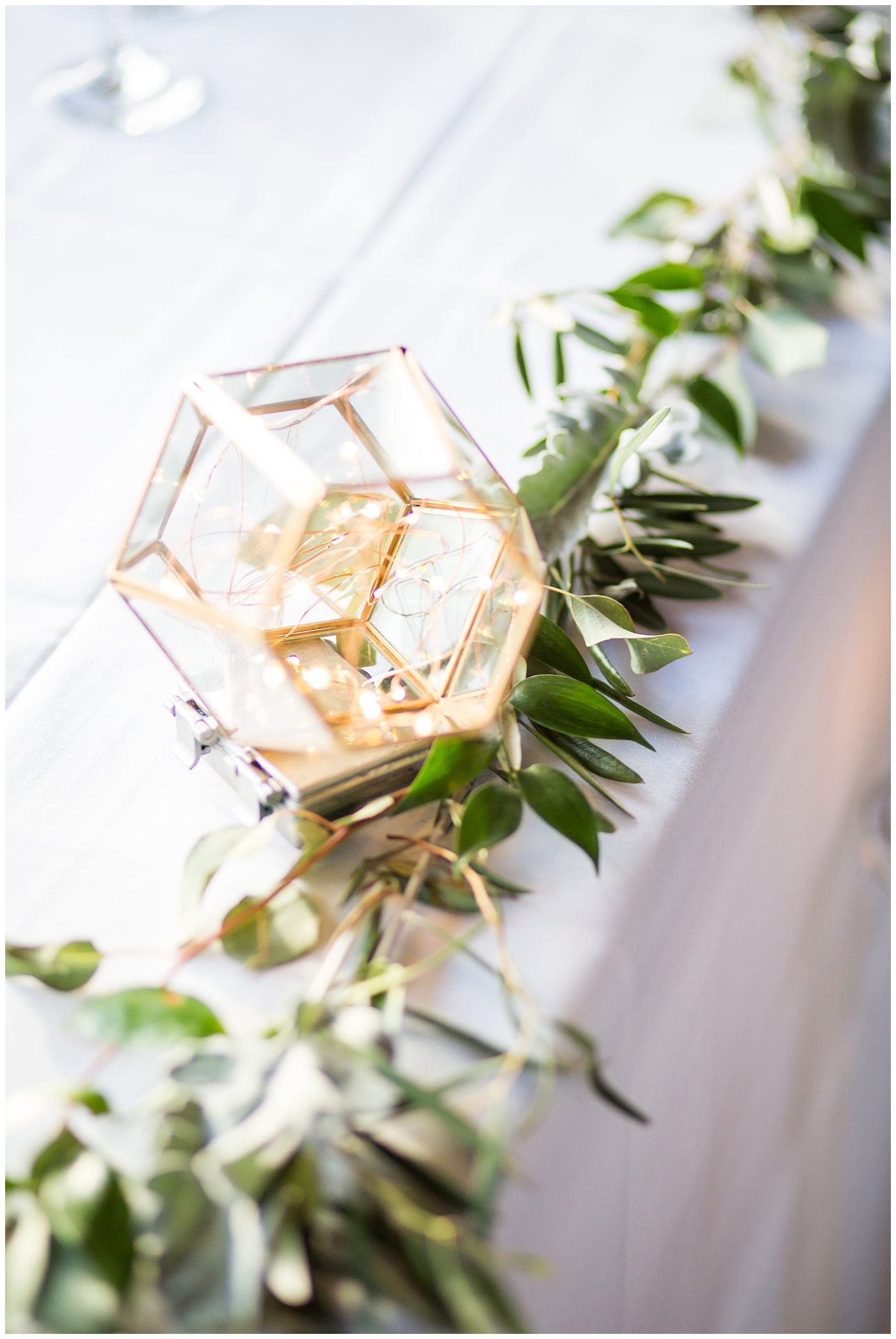 geometric terranium on mirror with glass vase with greenery and succulents with white table number and wood chairs in ballroom wedding reception details