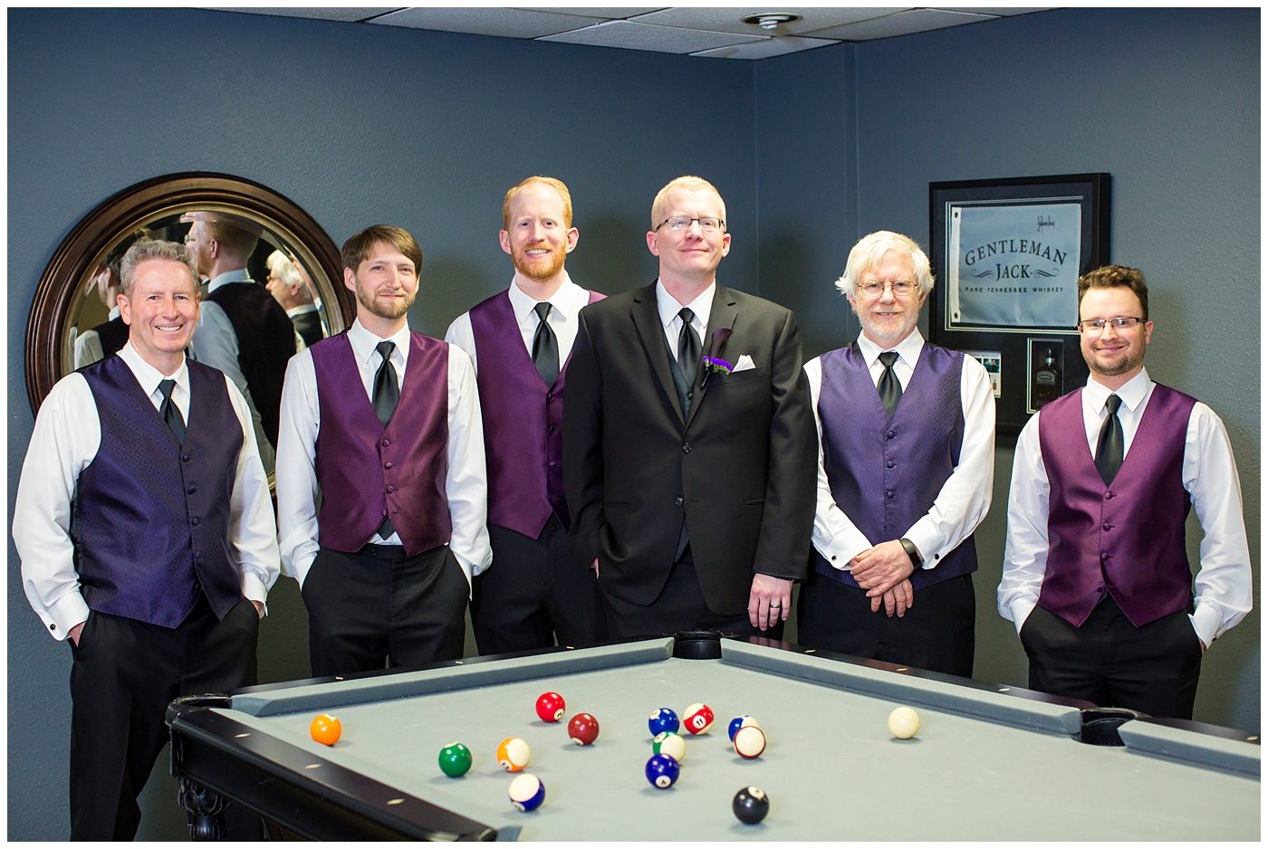 groom in black suit with purple calla lilly boutonniere with groomsmen in black suits with plum vests getting ready on wedding day