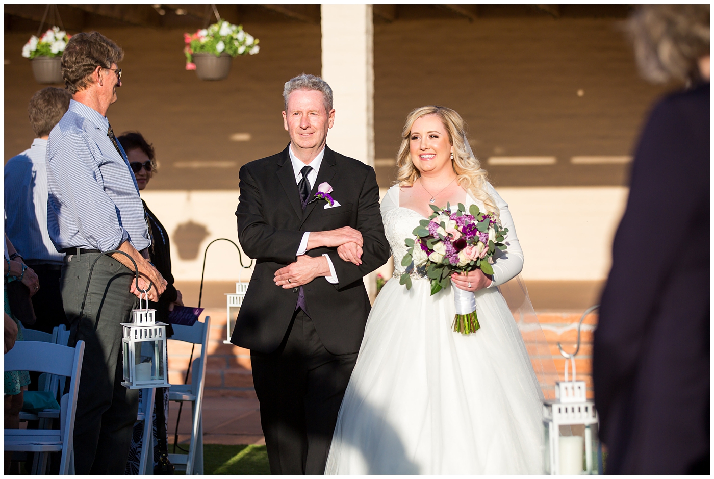 blonde bride in long sleeve wedding dress with purple and white flower bouquet walking down aisle with father at wedding ceremony