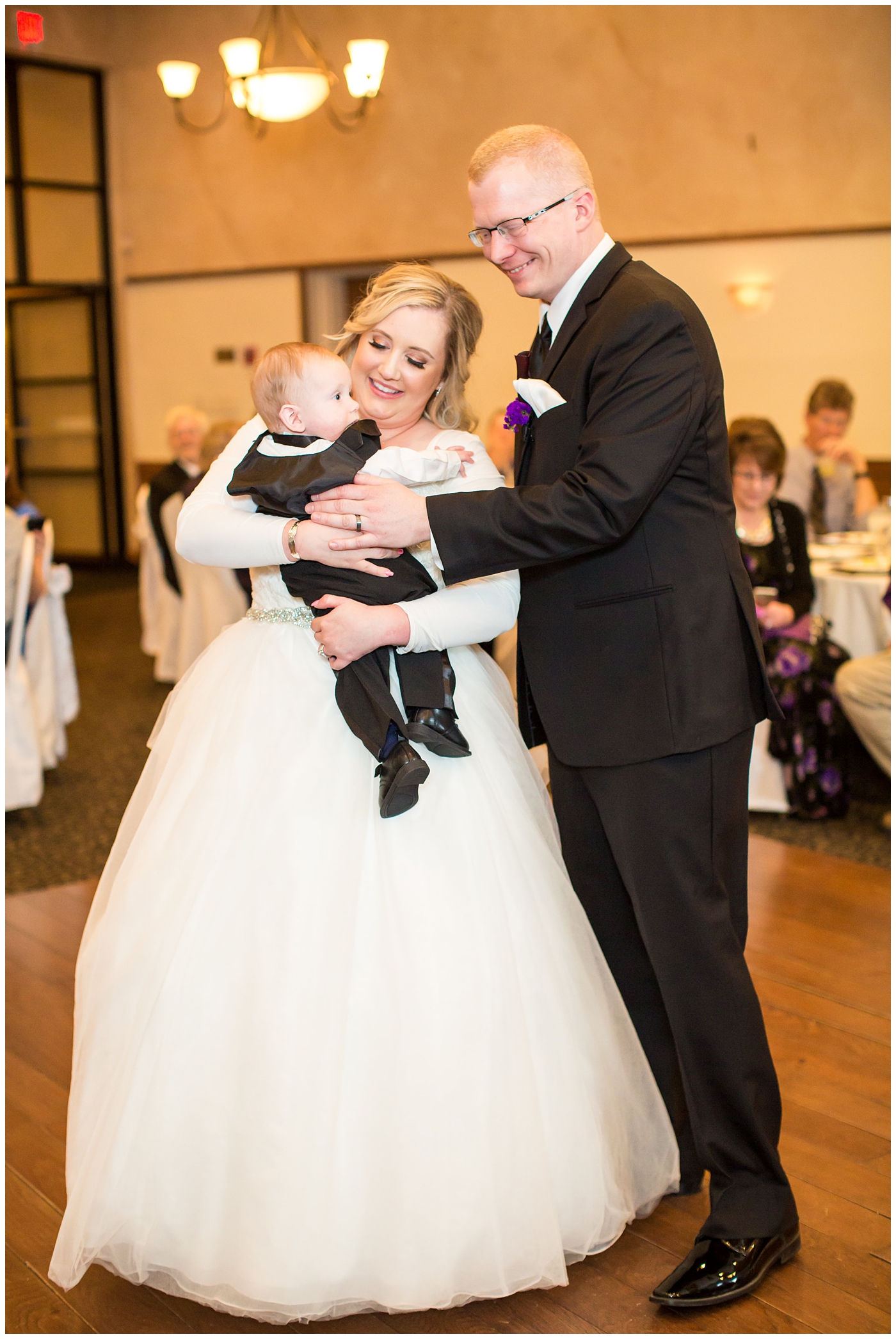 blonde bride in long sleeve wedding dress with purple and white flower bouquet and groom in black suit with purple calla lilly boutonniere wedding day first dance in ballroom reception
