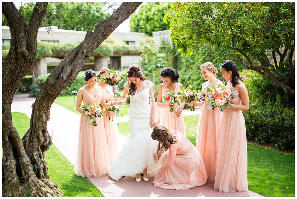 bride in matthew christopher wedding dress with cap sleeves with white, pink and orange ranunculus flowers and greenery bouquet with bridesmaids in blush wedding dresses getting ready on wedding day in front of Arizona Biltmore