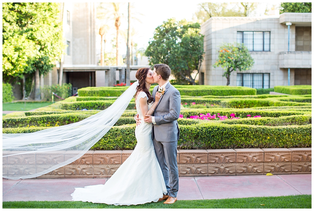 bride in matthew christopher wedding dress with cap sleeves with white, pink and orange ranunculus flowers and greenery bouquet with groom in light gray suit with tie wedding day portrait at Arizona Biltmore