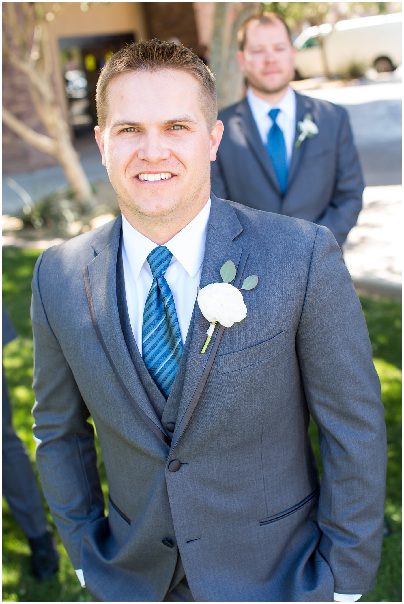 groom in light gray suit with blue tie and white rose boutonniere with groomsmen in gray suits with ties wedding day bridal party 
