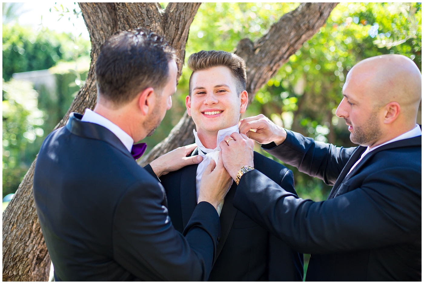 groom in black suit with purple bowtie with black and white feather getting ready with groomsmen on wedding day