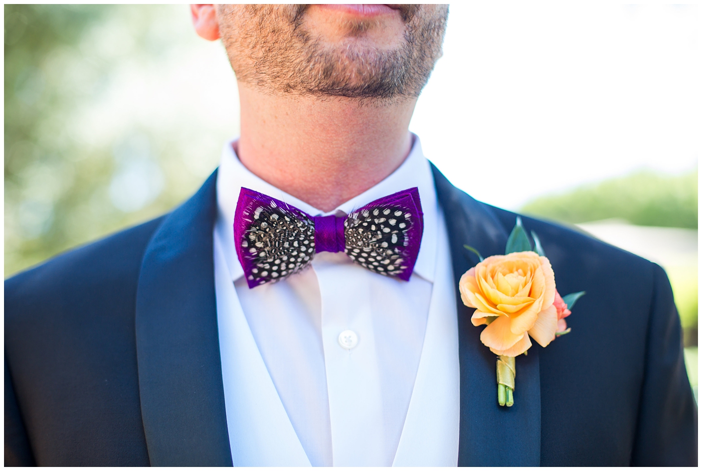 groom in black suit with purple bowtie with black and white feather and orange peony boutonniere wedding day portrait 