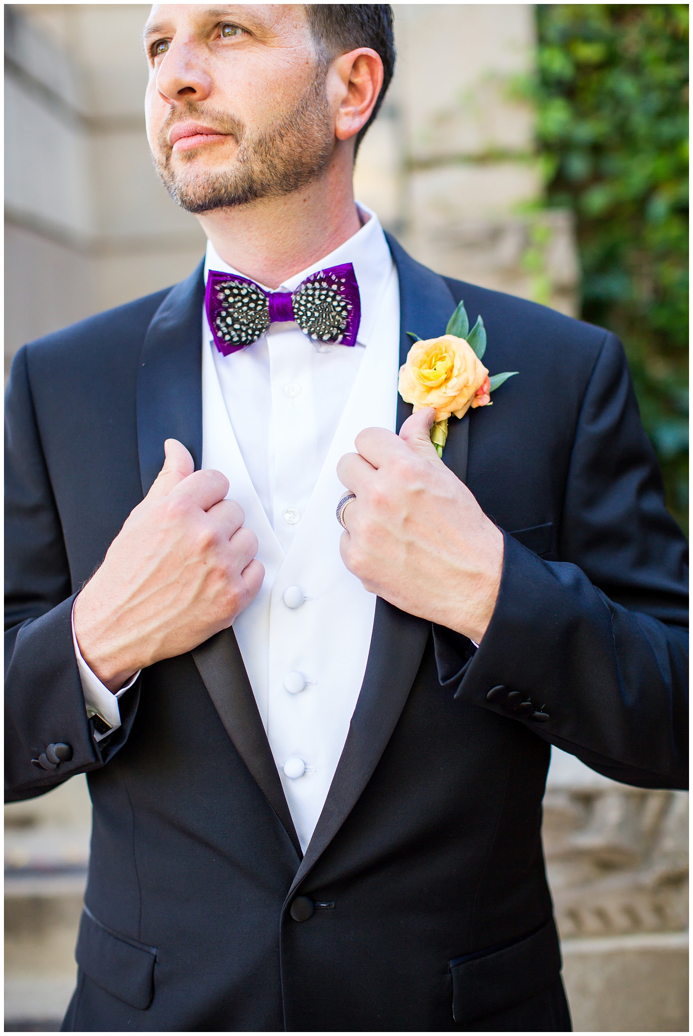 groom in black suit with purple bowtie with black and white feather with orange peony boutonniere wedding day portrait