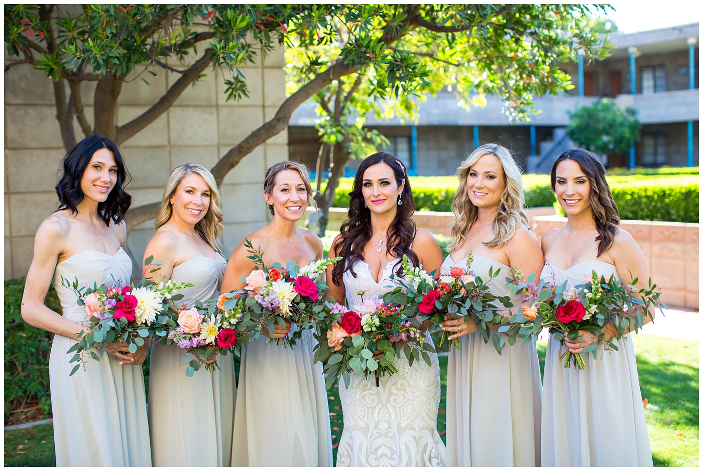 brunette bride in wedding dress with thin straps with bright color roses, dahlia, snap dragons loose bouquet with bridesmaids in champagne long dresses wedding day bridal party portrait 