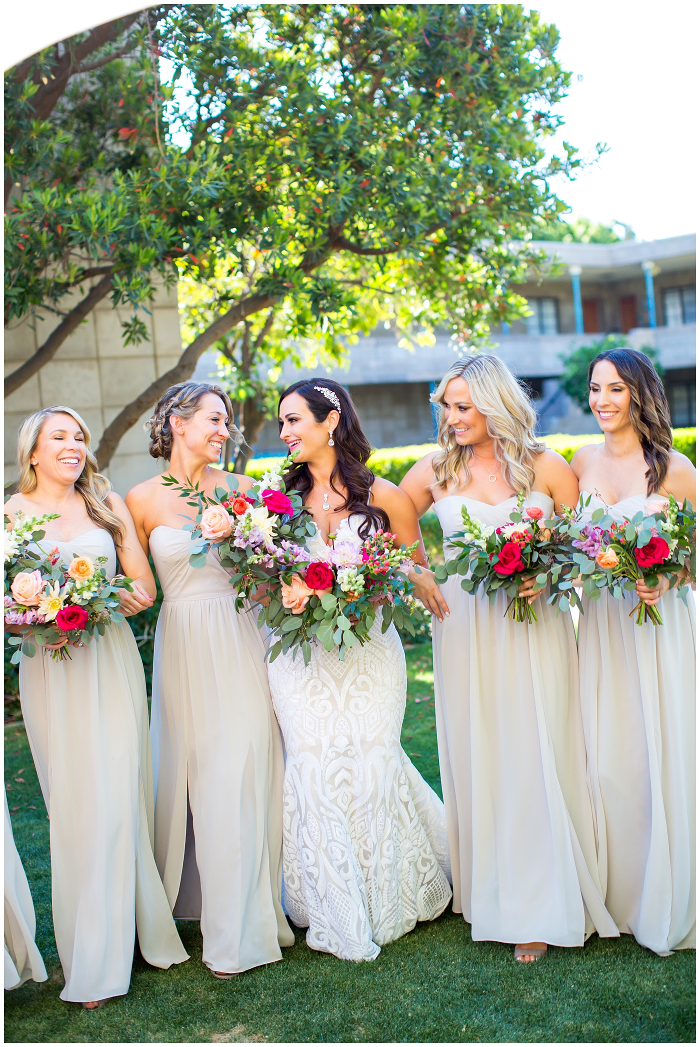 brunette bride in wedding dress with thin straps with bright color roses, dahlia, snap dragons loose bouquet with bridesmaids in champagne long dresses wedding day bridal party portrait 