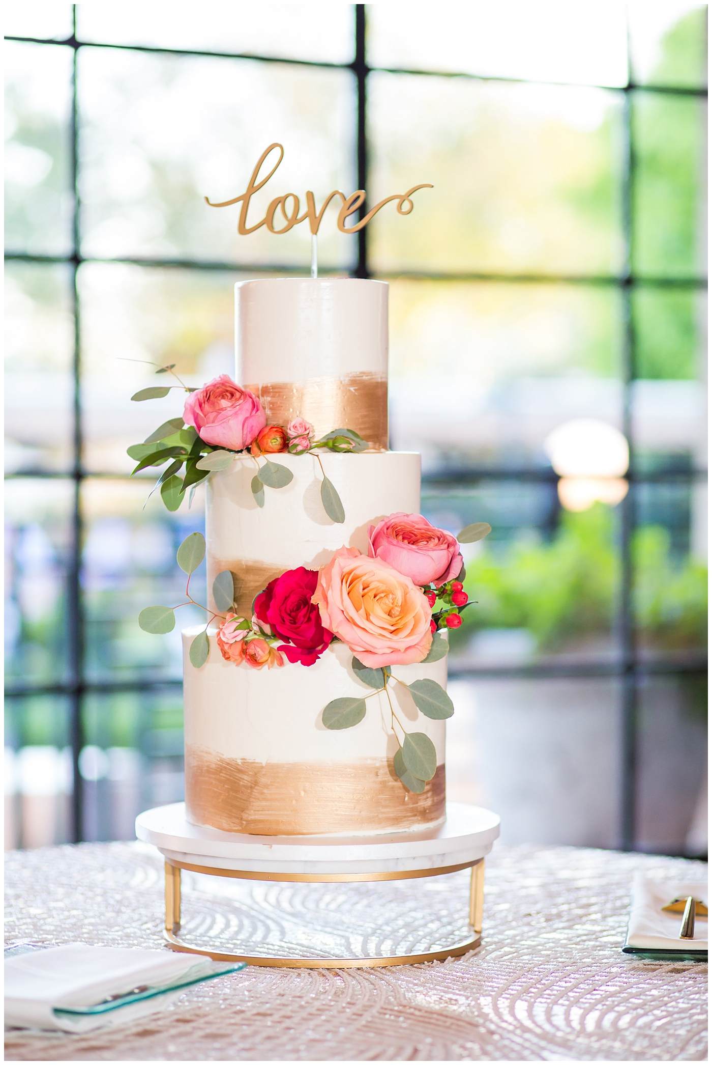 three tier wedding cake with gold foil and pink and orange peony design with cutout gold love topper wedding day detail