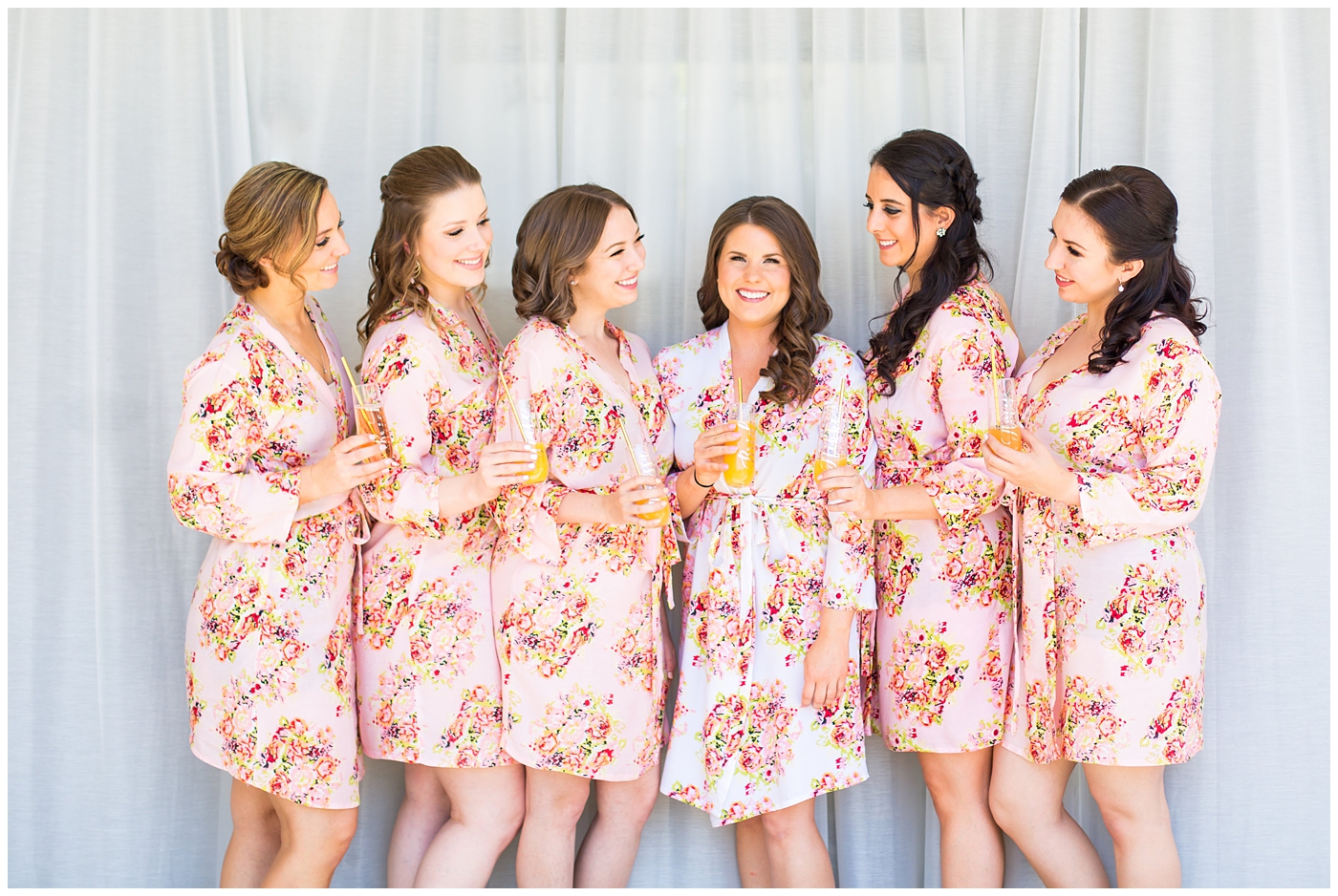 bride in white robe with pink flowers with bridesmaids in pink with flower robes getting ready on wedding day