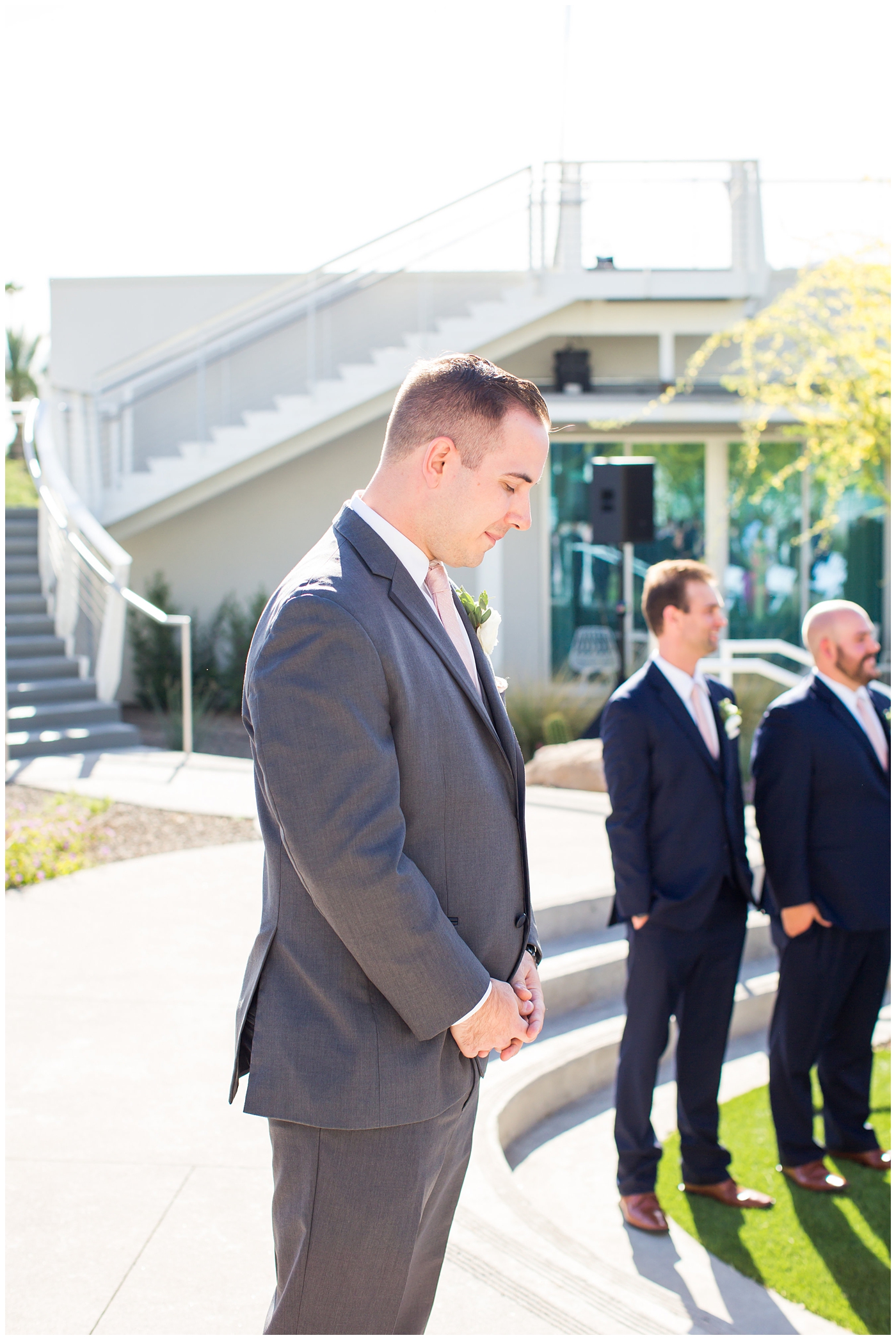 groom in gray suit with pink tie and ranunculus boutonniere waiting for bride to walk down the aisle at outdoor wedding ceremony
