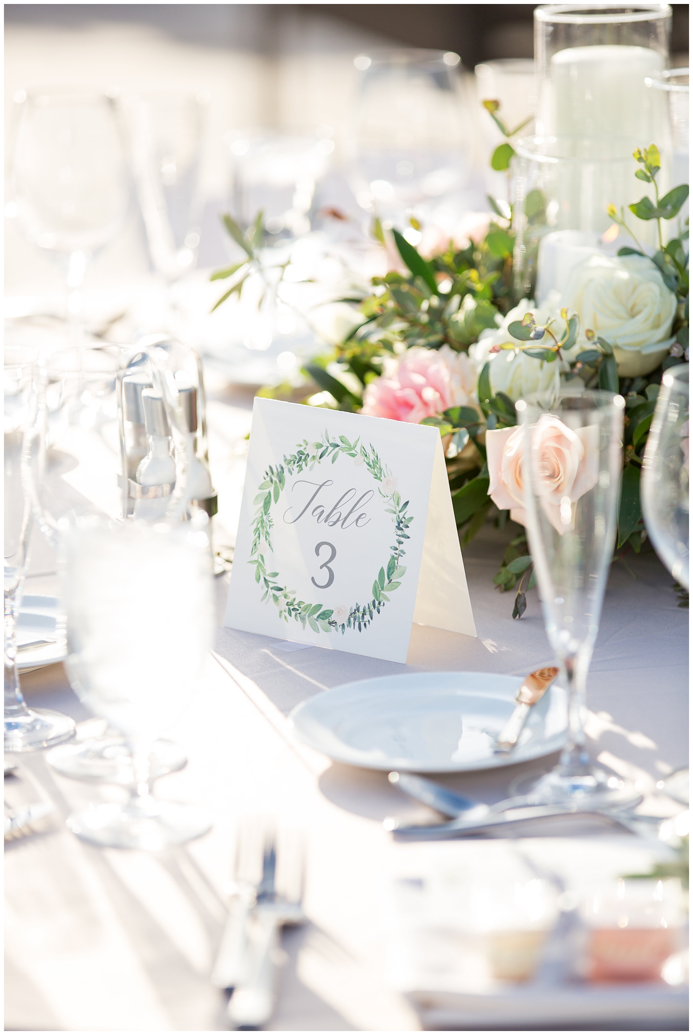 table number with green watercolor on blush linen with floral centerpiece with greenery white, blush, and soft pink roses with candles in the middle outdoor rooftop wedding reception detail