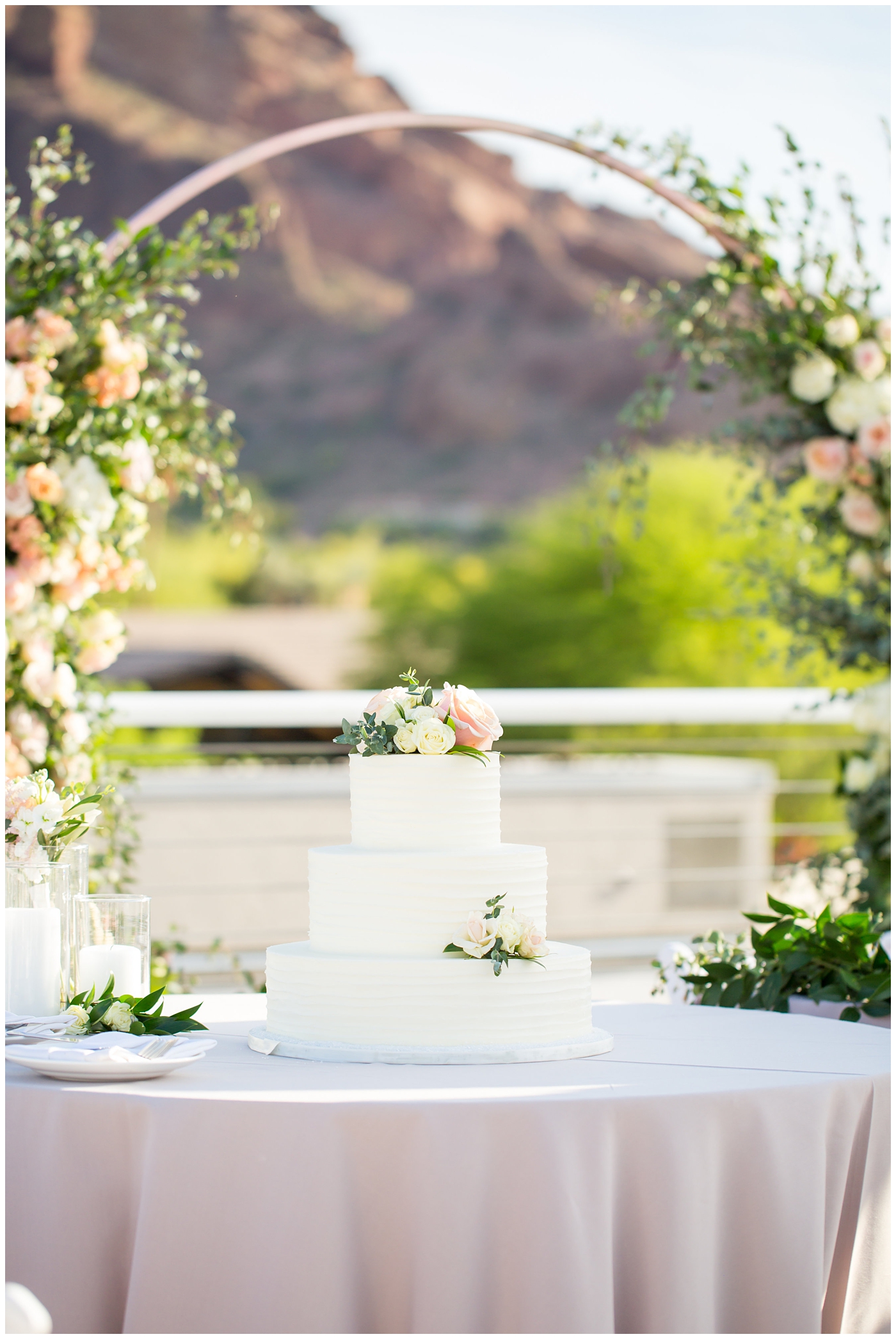 unique circle arch for ceremony with wildflowers in blush and white with greenery at outdoor rooftop wedding reception with mountain in background and three tier wedding cake with white frosting and flowers for decoration