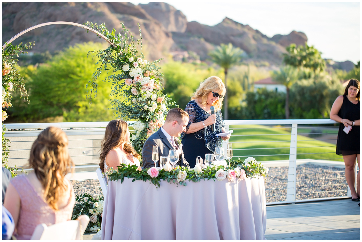 mother of groom giving speech with unique circle arch for outdoor rooftop wedding reception with wildflowers in blush and white with greenery with mountain in background