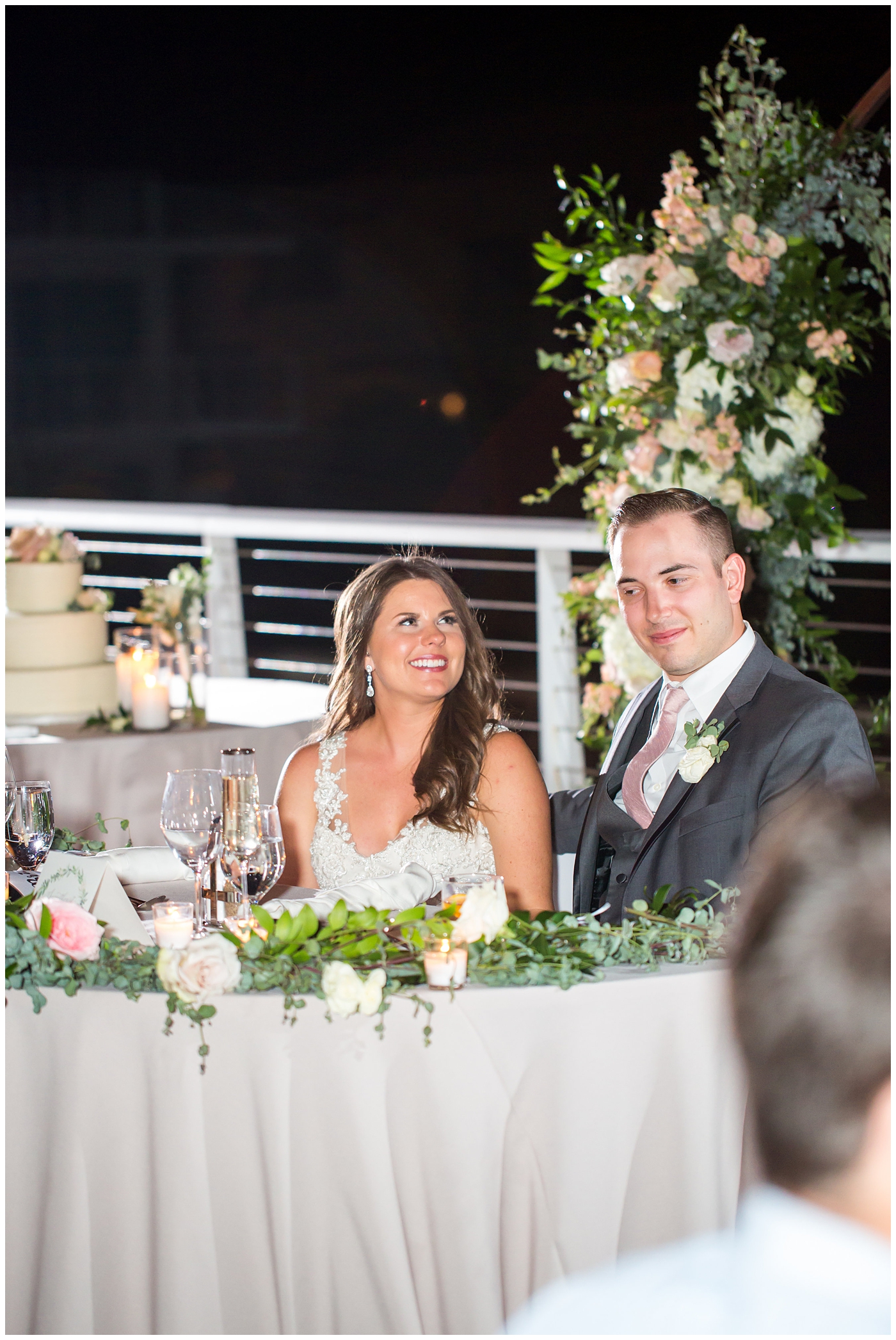 couple during speech with unique circle arch for outdoor rooftop wedding reception with wildflowers in blush and white with greenery with twinkle lights stranded above