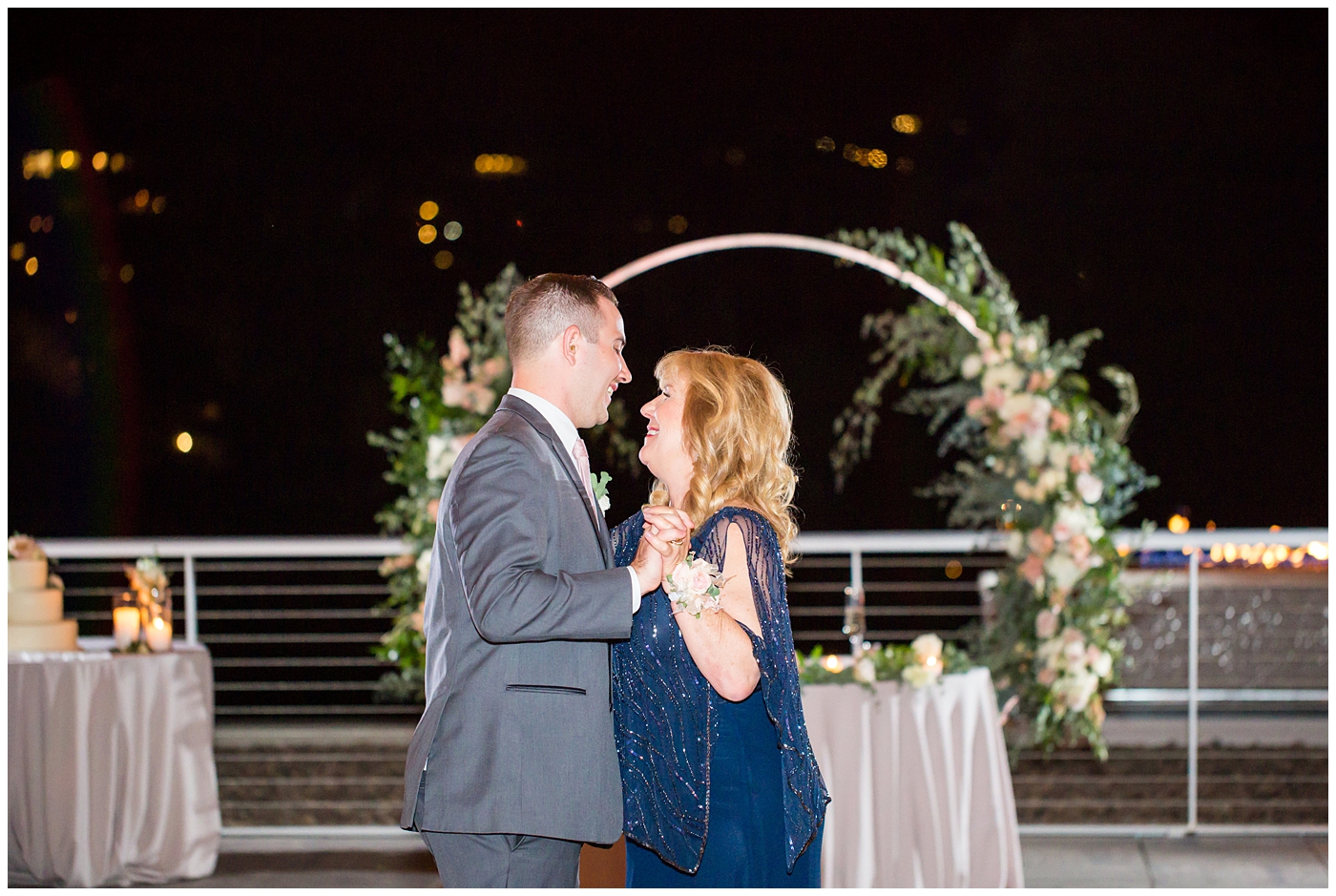 mother and son dance with unique circle arch for outdoor rooftop wedding reception with wildflowers in blush and white with greenery with twinkle lights stranded above