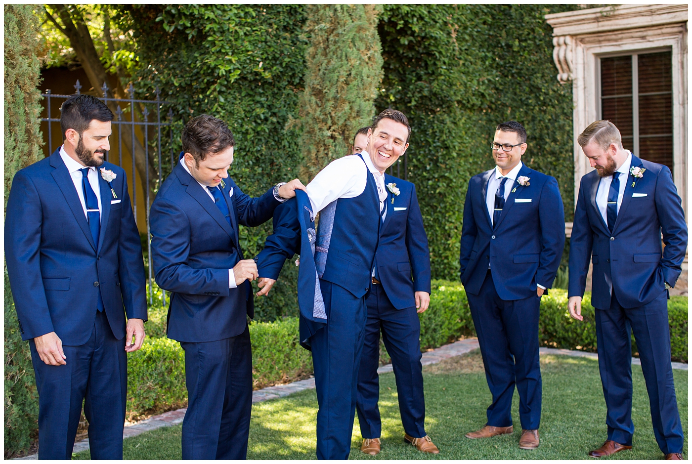 groom in blue suit with blush rose boutonniere getting ready on wedding day with groomsmen in blue suits
