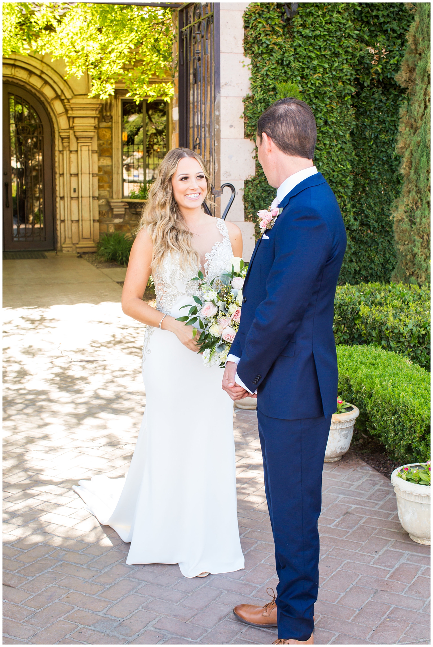 bride in lillian lottie couture strapped beaded wedding dress with organic blush, white and greenery bouquet with groom in blue suit with rose boutonniere wedding day first look portrait 