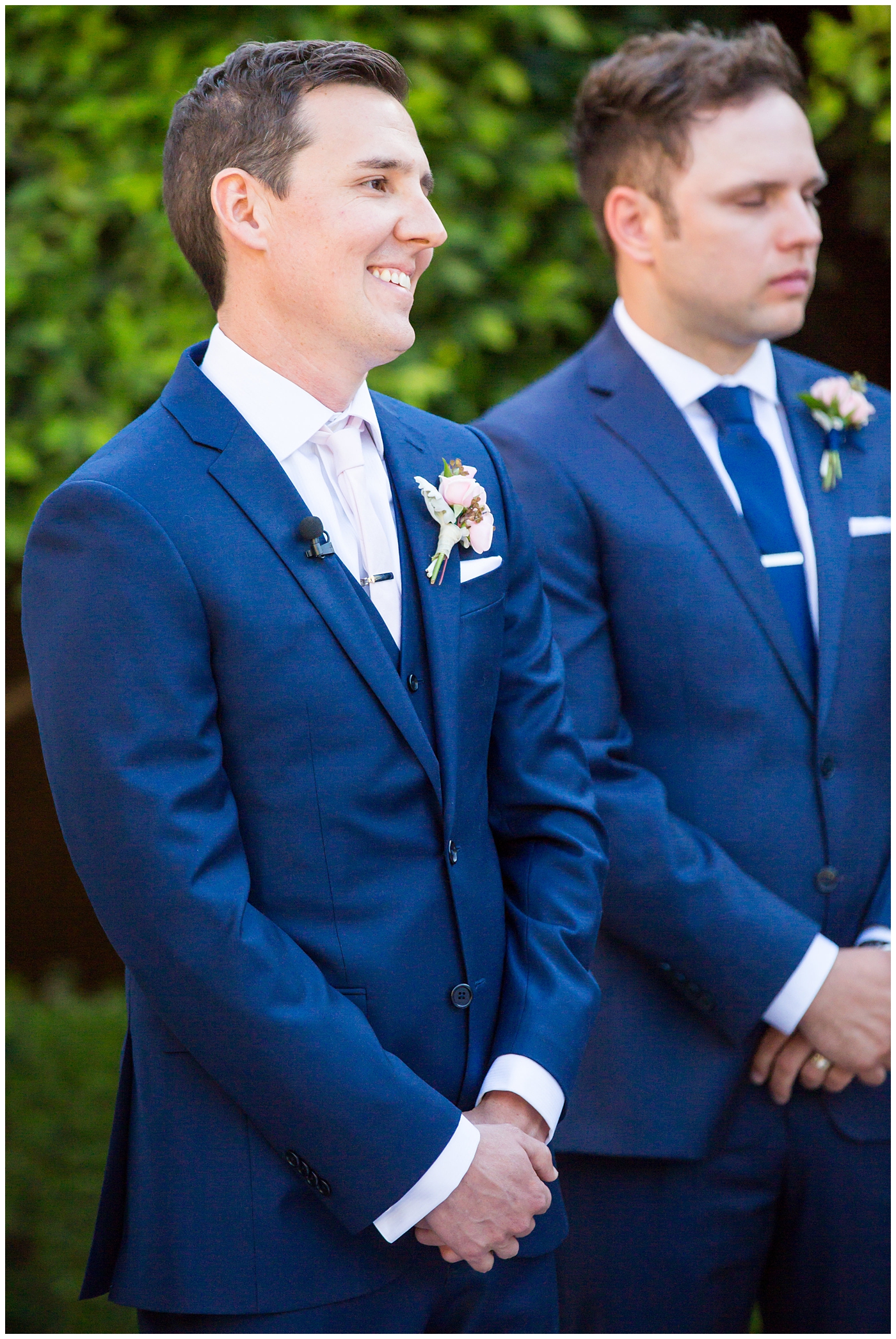 groom in blue suit with blush rose boutonniere seeing bride walk down outdoor wedding aisle