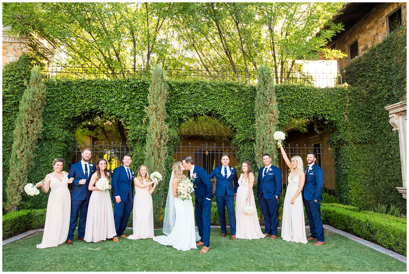 bride in lillian lottie couture strapped beaded wedding dress with bridesmaids in long blush dresses with groom in blue suit with blush rose boutonniere with groomsmen in blue suits wedding day bridal party portrait