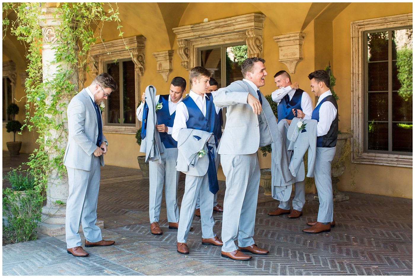 groom in grey suit with blue tie and white rose boutonniere and groomsmen in grey suits with royal blue vests and ties getting ready on wedding day