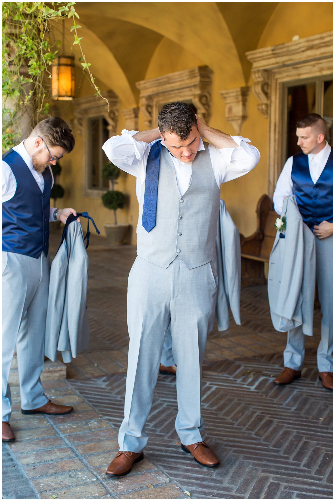 groom in grey suit with blue tie and white rose boutonniere and groomsmen in grey suits with royal blue vests and ties getting ready on wedding day