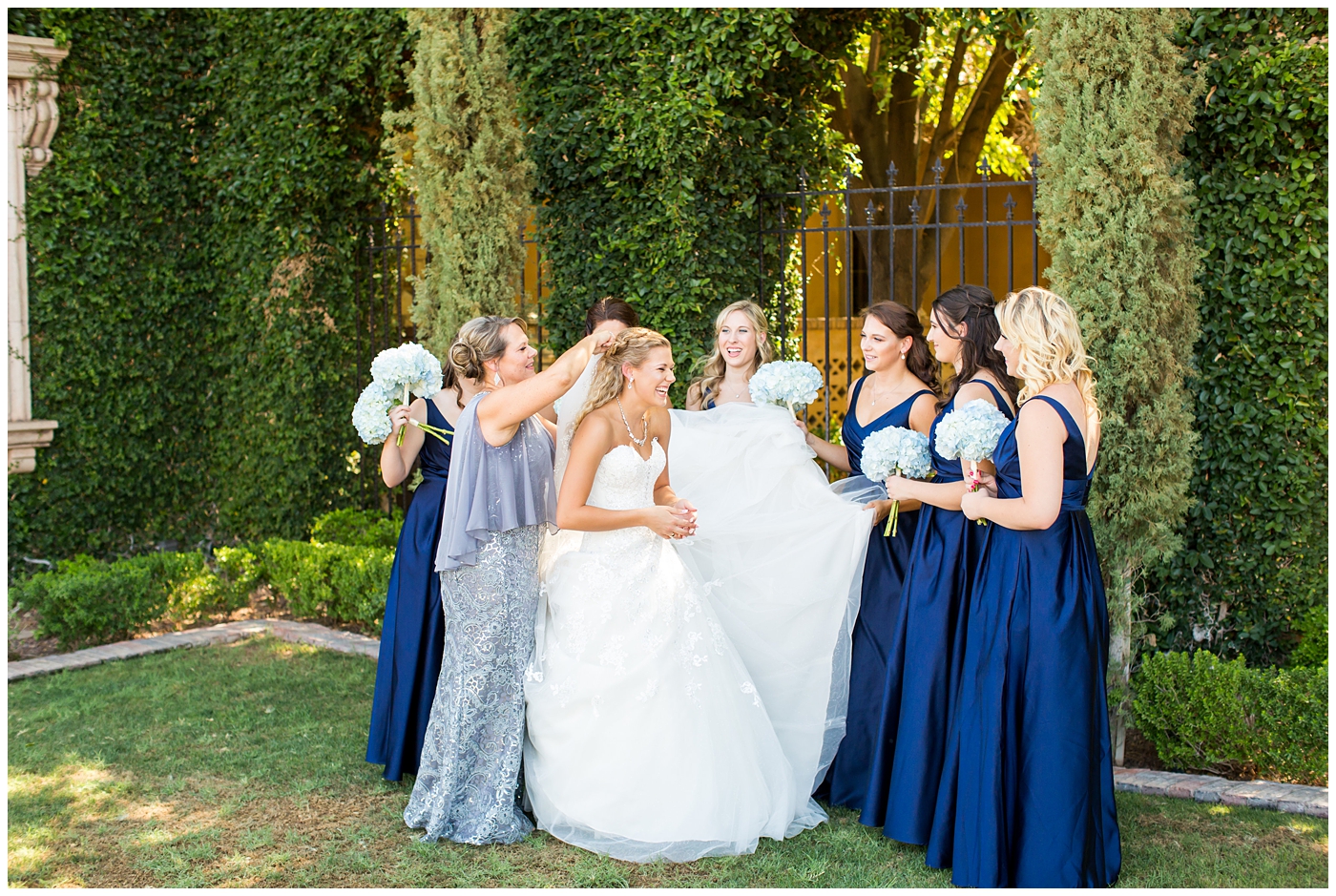 bride in strapless lace dress with white flower bouquet with roses and hydrangeas with bridesmaids in royal blue long dresses with blue hydrangeas bouquets getting ready on wedding day