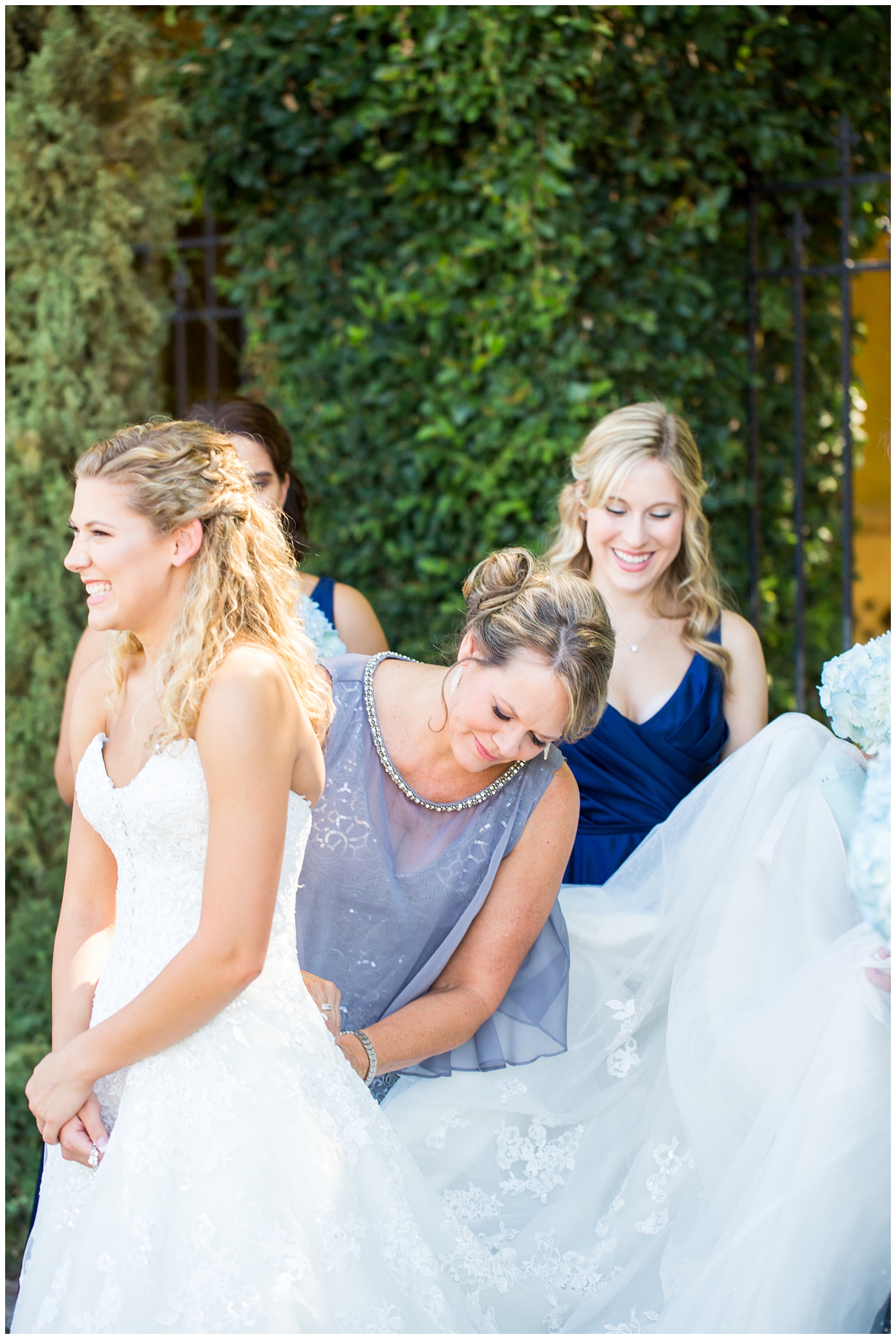 bride in strapless lace dress with white flower bouquet with roses and hydrangeas with bridesmaids in royal blue long dresses with blue hydrangeas bouquets getting ready on wedding day