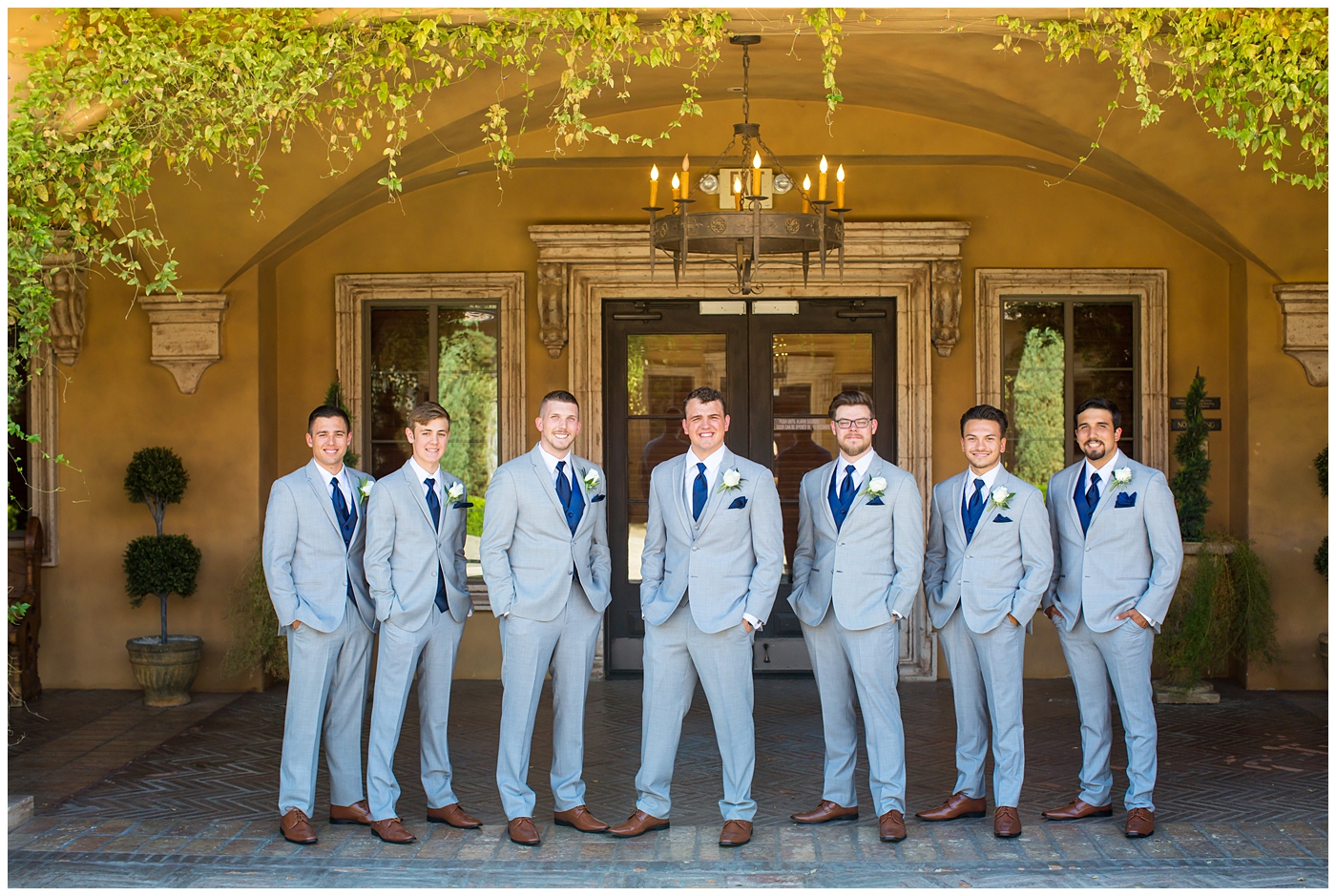 groom in grey suit with blue tie and white rose boutonniere and groomsmen in grey suits with royal blue vests and ties on wedding day