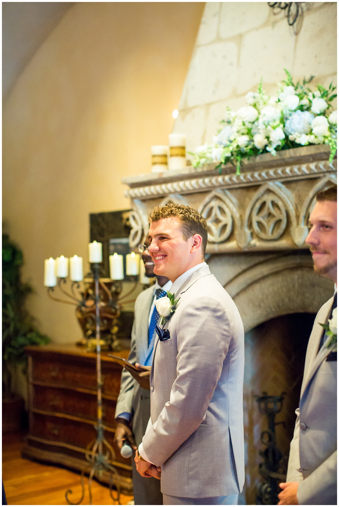 groom in grey suit with blue tie and white rose boutonniere seeing bride walking down the aisle for the first time on wedding day