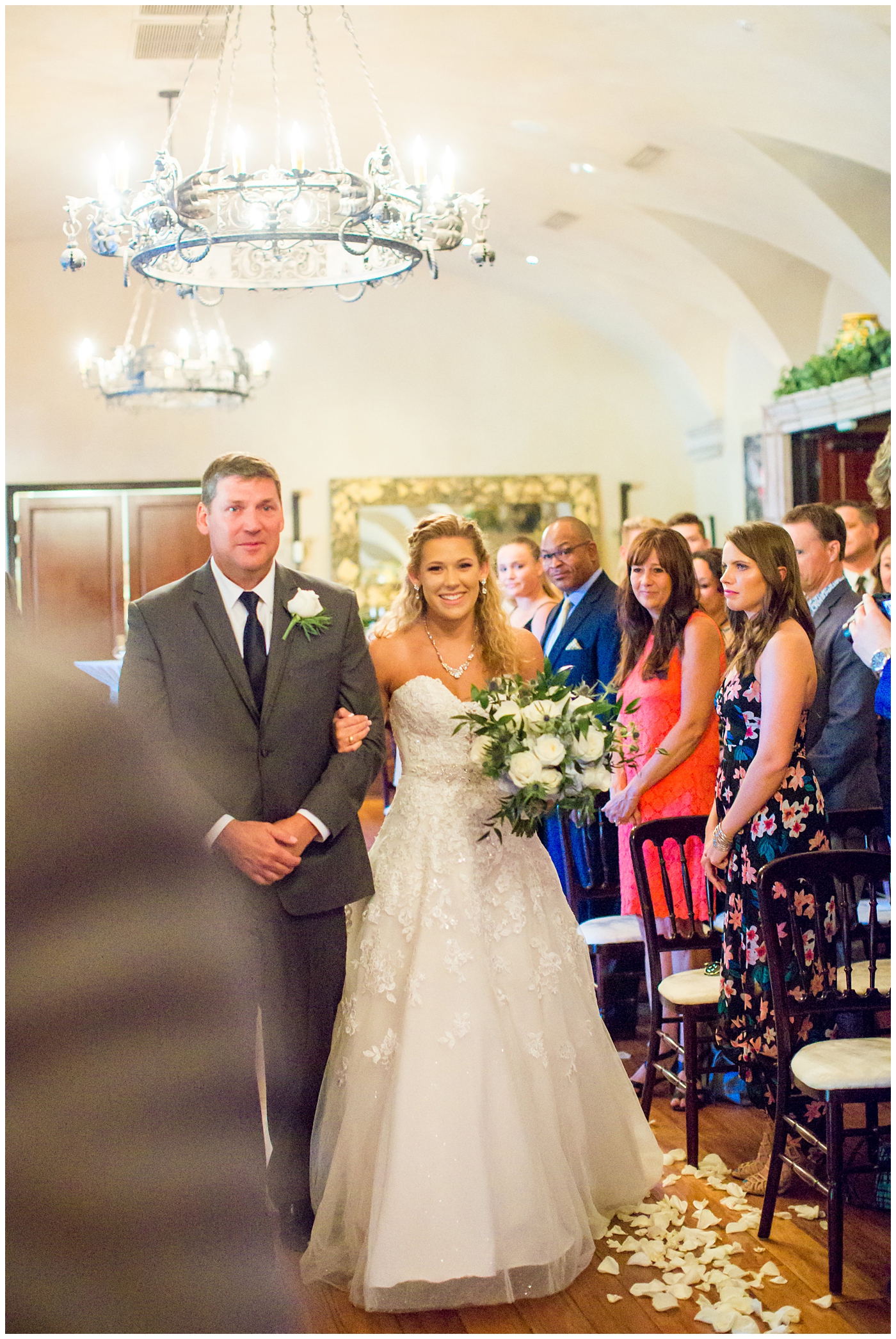 bride in strapless lace dress with white flower bouquet with roses and hydrangeas walking down aisle in inside ceremony with father on wedding day
