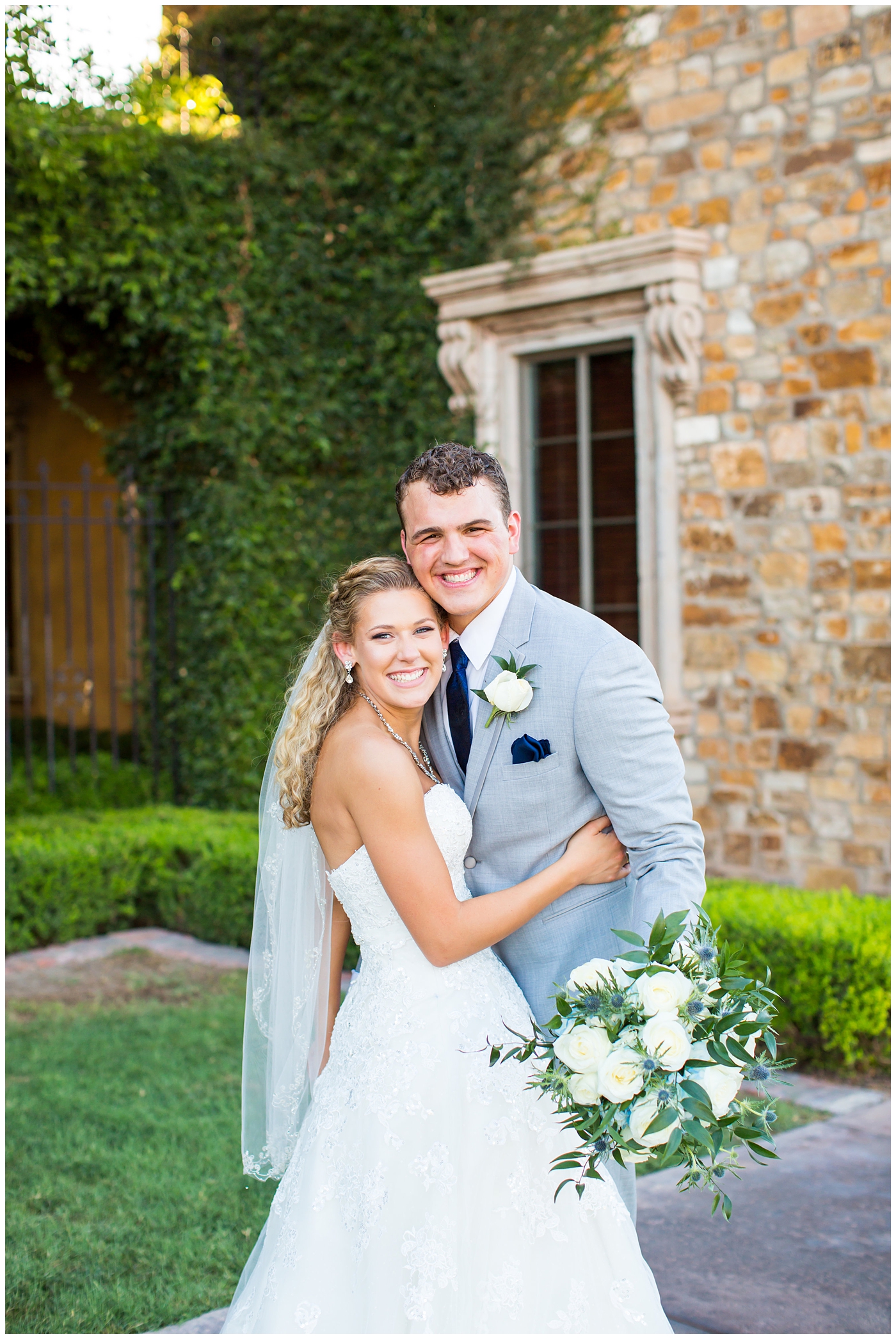 bride in strapless lace dress with white flower bouquet with roses and hydrangeas with groom in light grey suit with blue tie with white rose boutonniere wedding day portrait 
