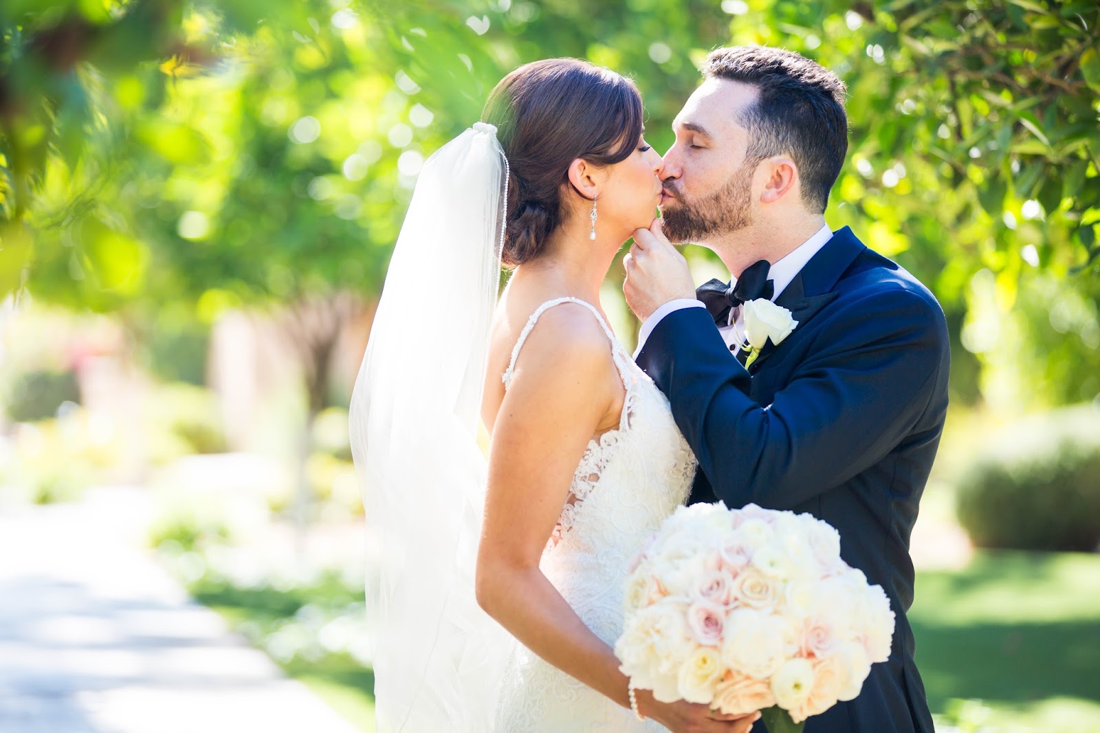 classic romantic bride with white and blush roses wedding bouquet kissing groom in navy suit at Omni Montelucia