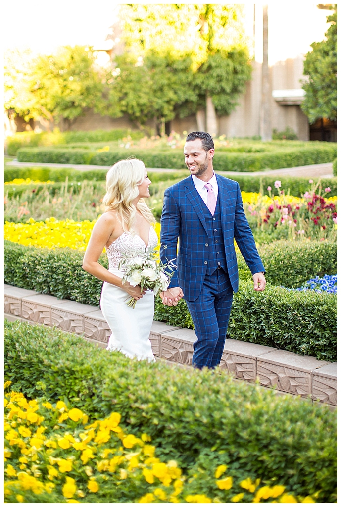 bride in two piece wedding dress and groom in custom blue suit in the garden at Arizona Biltmore