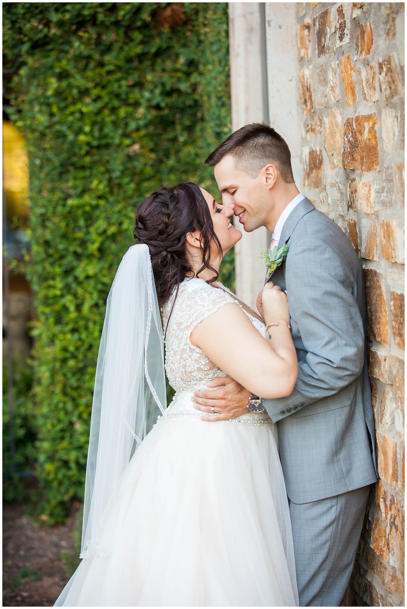 Bride in sleeved white dress and groom in gray jacket kissing