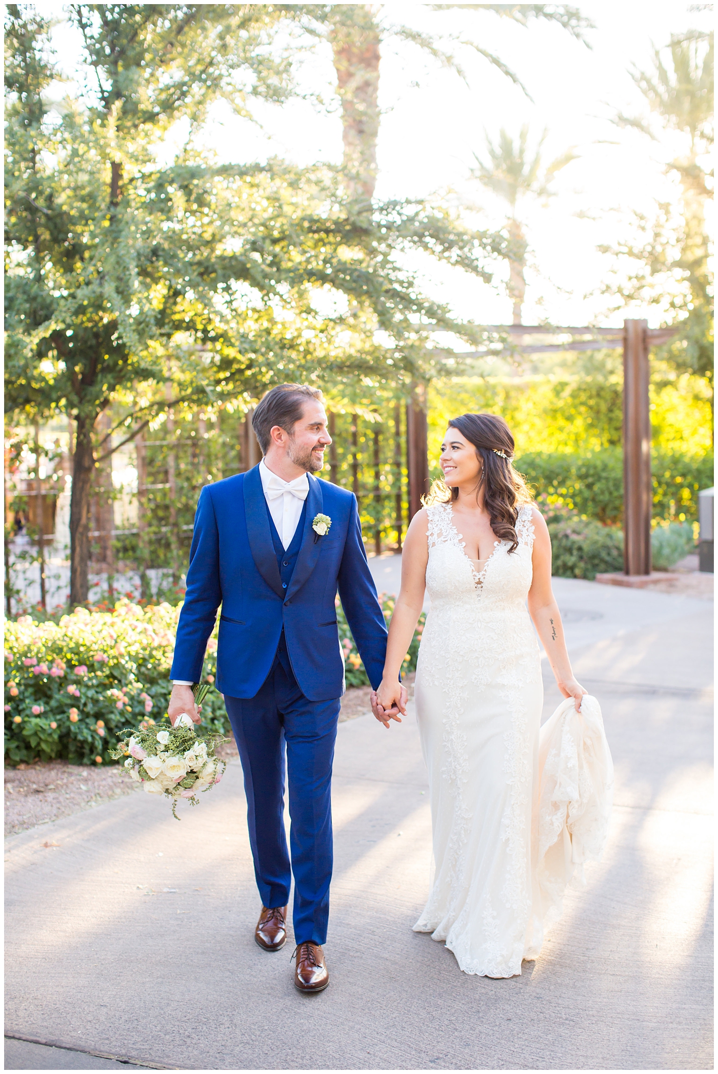 Bride in Justina Alexander dress with groom in custom blue suit holding hands 