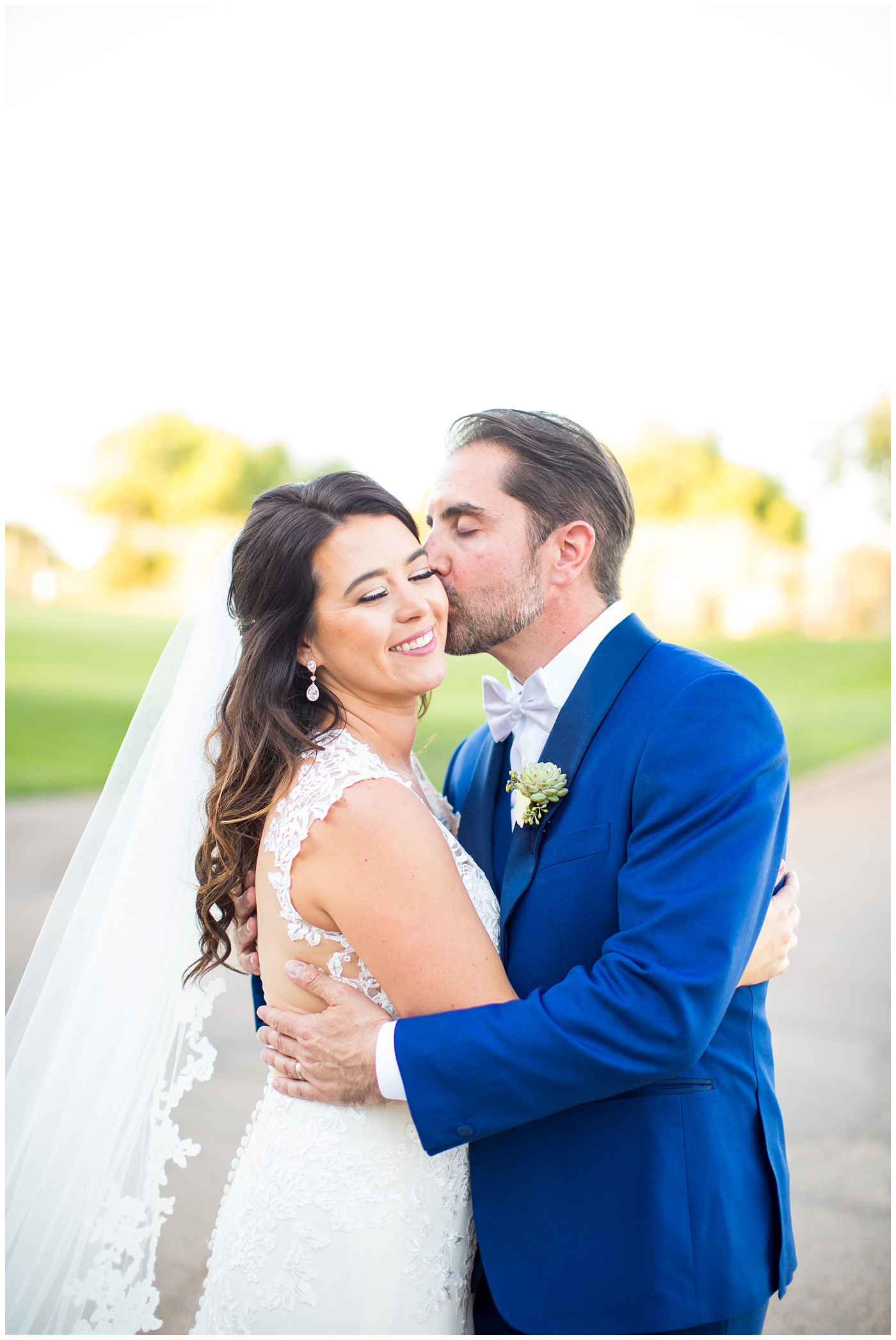 Bride in Justina Alexander dress with groom in custom blue suit kissing her cheek
