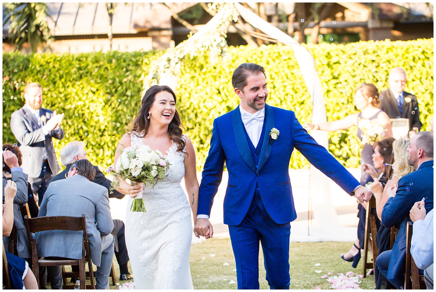 Bride in Justina Alexander dress with groom in custom Brother's Tailors blue suit walking down aisle
