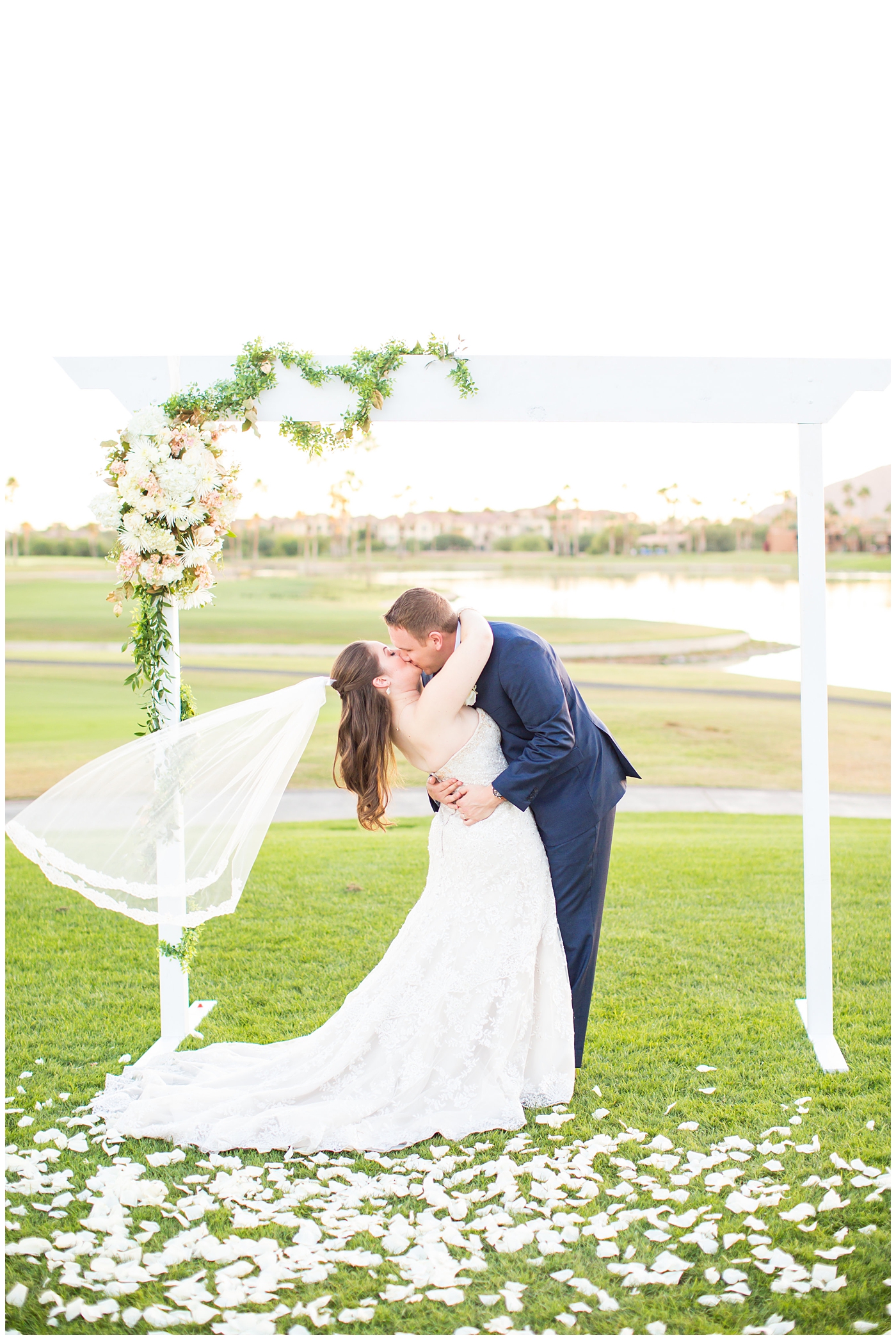 bride in lillian lottie couture wedding dress with white rose bouquet and groom in navy blue suit from men's warehouse bride and groom wedding portrait under arch on golf course