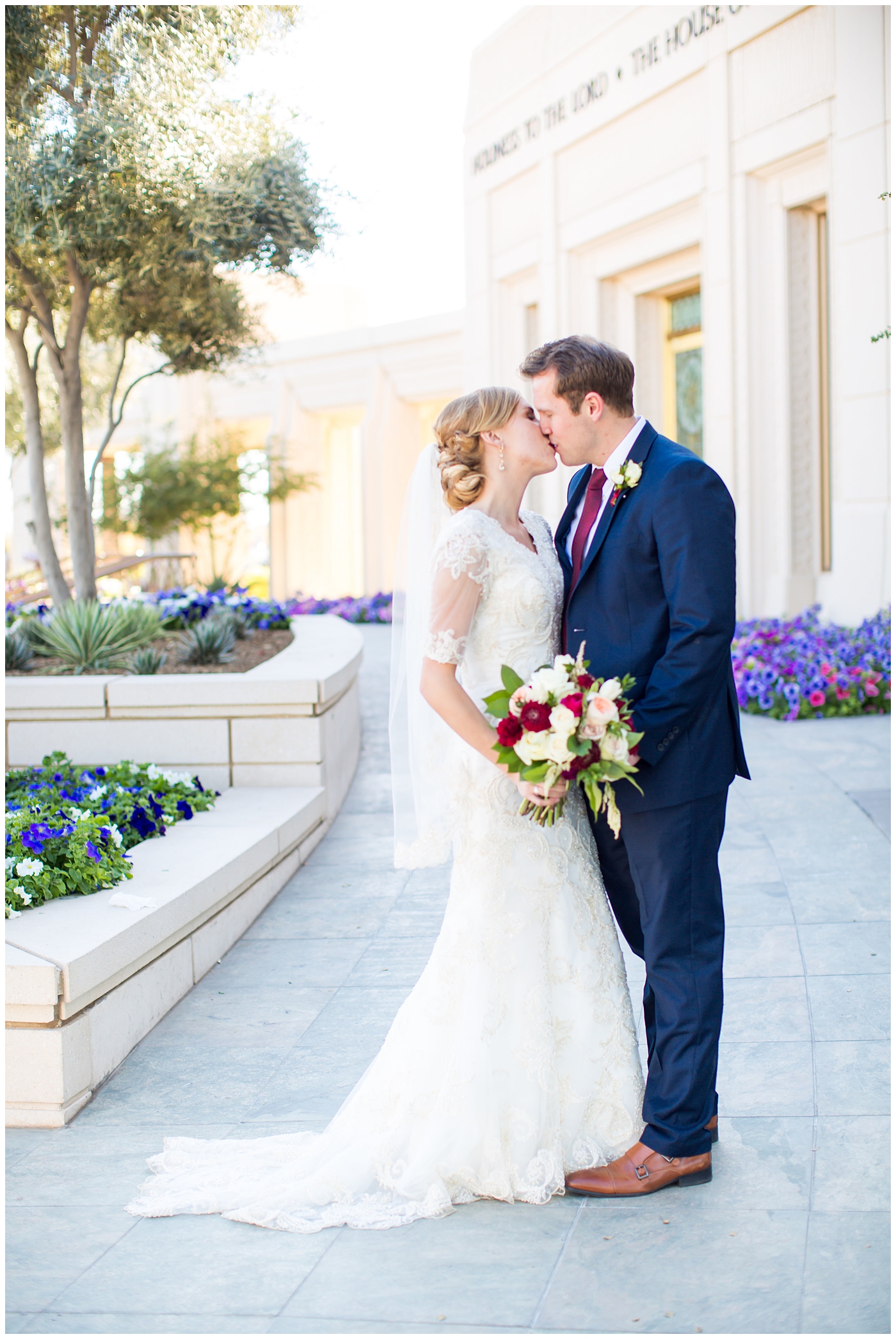 bride in sleeved lace dress with burgundy, white, and green wedding bouquet and groom in navy suit with burgundy tie wedding day portrait at Gilbert LDS temple
