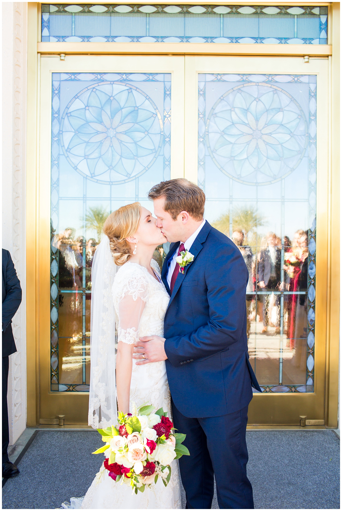 bride in sleeved lace dress with burgundy, white, and green wedding bouquet and groom in navy suit with burgundy tie wedding day grand exit at Gilbert LDS temple