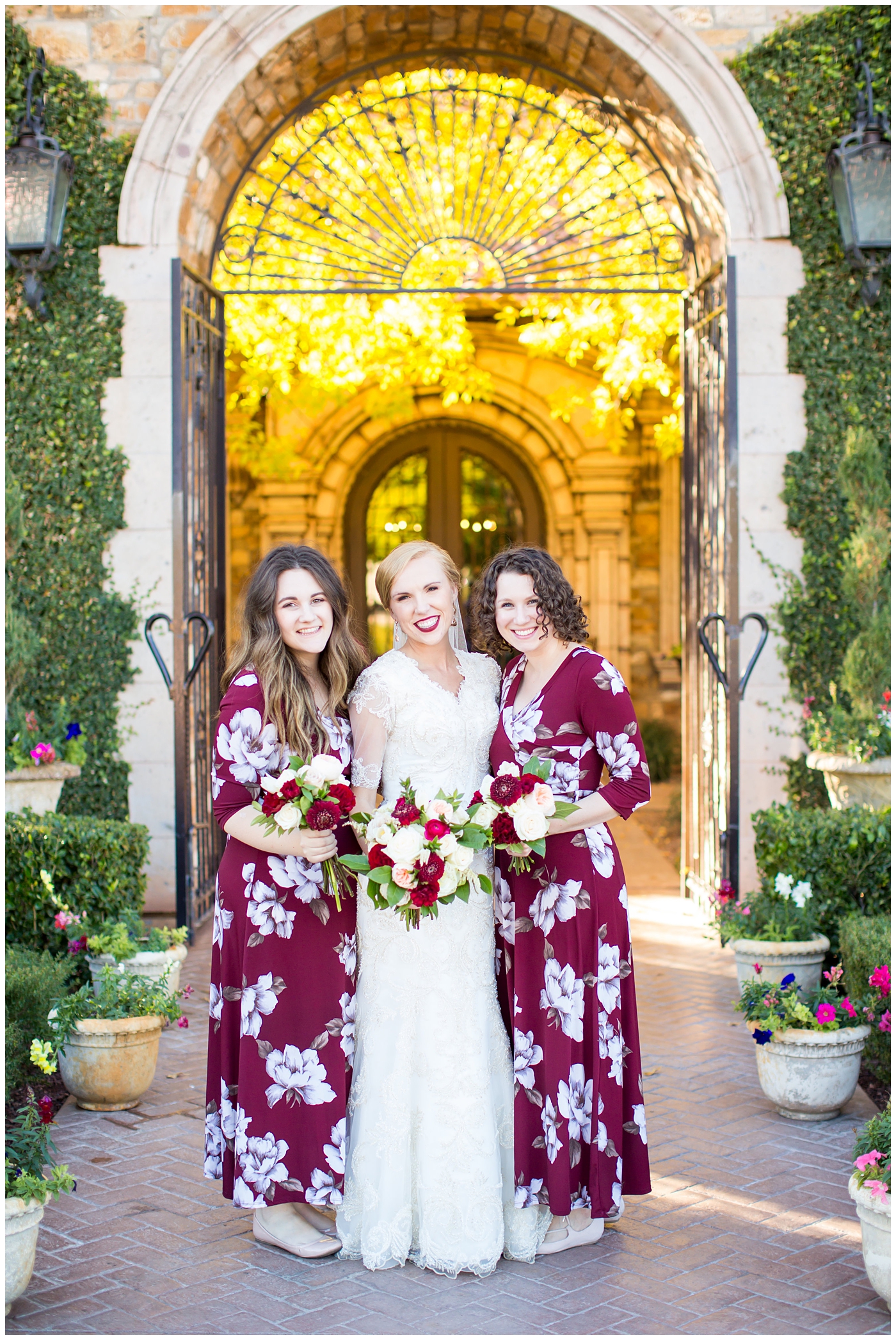bride in sleeved lace dress with burgundy, white, and green wedding bouquet with bridesmaids in long sleeve burgundy and floral dresses wedding day portrait at Villa Siena