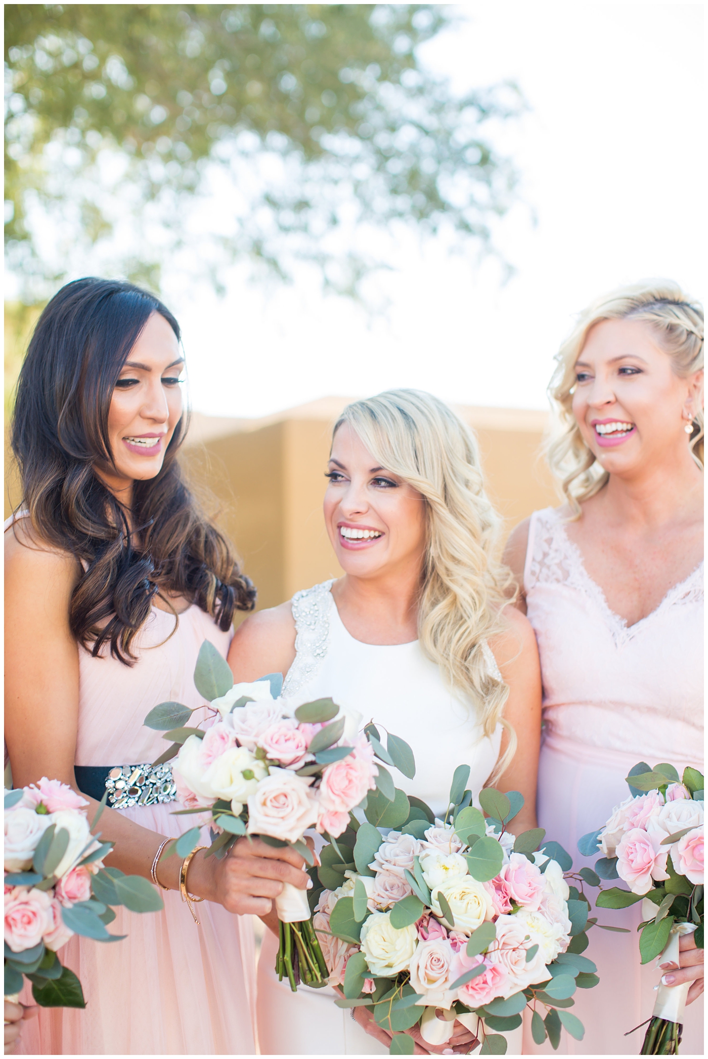 gorgeous bride with side swept hair in racerback pronovias dress and blush pink, white rose and eucalyptus greenery wedding bouquet with bridal party bridesmaids in blush pink dresses on wedding day