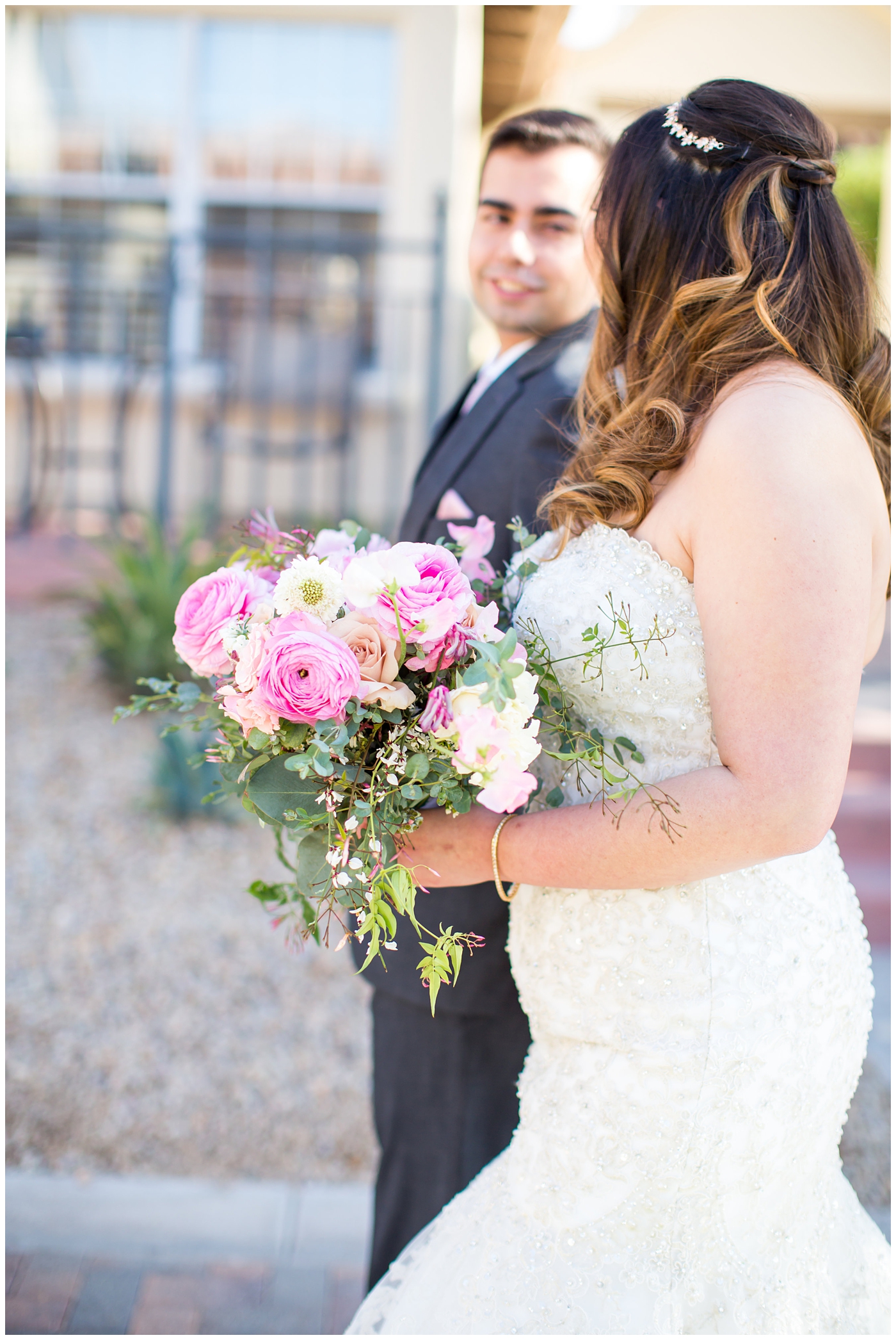 bride in strapless wedding dress with beads and shiny sparkle tool holding pink peony, roses, light coral rose and loose greenery bridal bouquet with groom in gray suit with silver tie on wedding day portrait