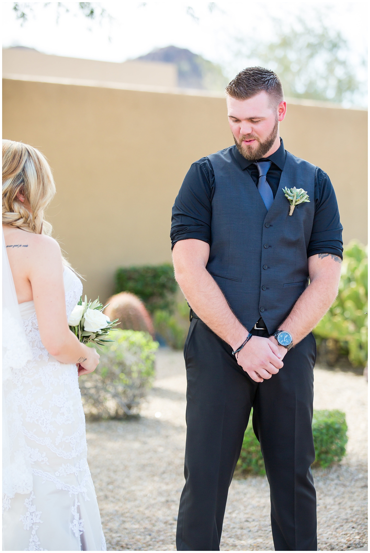 bride with fishtail braid and strapless dress with white rose and greenery bouquet with groom in black pants and vest and tie with rolled up shirt sleeves with succulent boutonniere wedding day first look portrait