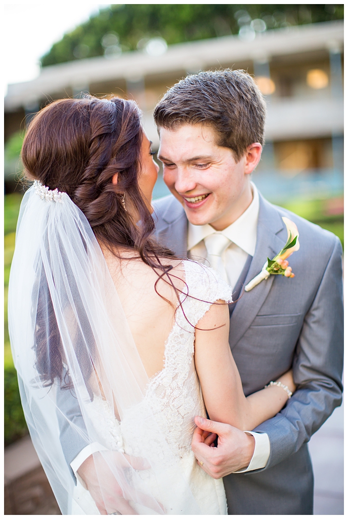 bride in matthew christopher wedding dress with cap sleeves with white, pink and orange ranunculus flowers and greenery bouquet with groom in light gray suit with tie wedding day portrait at Arizona Biltmore